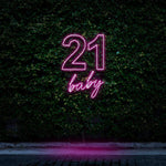 Bright pink neon sign displaying "21 Baby," glowing against a green leafy background, perfect for 21st birthday celebrations and trendy party decorations.