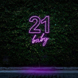 Pink and purple neon sign reading "21 Baby," glowing against a green leafy background, perfect for 21st birthday celebrations and party decorations.