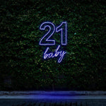 Purple neon sign displaying "21 Baby," glowing beautifully against a green leafy wall, perfect for 21st birthday celebrations and party decor.