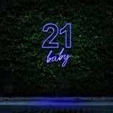 Purple neon sign displaying "21 Baby," glowing beautifully against a green leafy wall, perfect for 21st birthday celebrations and party decor.