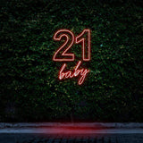 Bright red neon sign reading "21 Baby," glowing against a green leafy wall, perfect for 21st birthday celebrations and bold party decorations.