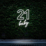 Bright white neon sign reading "21 Baby," glowing elegantly against a green leafy wall, ideal for 21st birthday celebrations and minimalist party decorations.