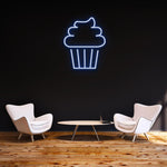 Blue cake LED neon sign on a dark background, enhancing a stylish room with elegant furniture and wooden flooring.