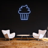 Blue cake LED neon sign on a dark background, enhancing a stylish room with elegant furniture and wooden flooring.