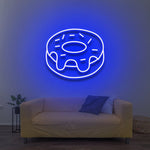 Blue donut LED neon sign for wall decor above a cozy yellow couch in a modern living room.