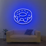 Blue donut LED neon sign for wall decor above a cozy yellow couch in a modern living room.