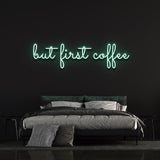 Green "But First Coffee" LED neon sign above a cozy bed setup on a black wall, great decor for coffee lovers and modern spaces.