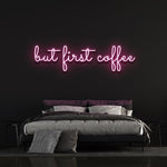 Hot pink "But First Coffee" LED neon sign displayed above a modern bedroom setup with a black wall background, perfect for coffee lovers.