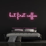 Hot pink "But First Coffee" LED neon sign displayed above a modern bedroom setup with a black wall background, perfect for coffee lovers.