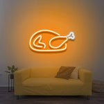 Chicken LED neon sign glowing in orange color, mounted on a wall above a yellow couch, ideal for home decor and restaurant ambiance lighting.