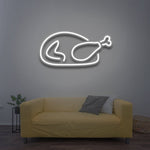 Chicken LED neon sign glowing in white color, placed on a gray wall above a yellow couch, suitable for modern living room and cafe lighting.