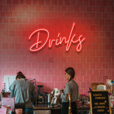 Red "Drinks" LED neon sign lighting up a modern cafe with vibrant pink wall tiles.