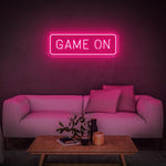 Pink GAME ON LED neon sign glowing in a modern living room with a white couch and decor.