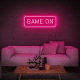 Pink GAME ON LED neon sign glowing in a modern living room with a white couch and decor.