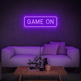 Purple GAME ON LED neon sign above a modern white couch with wooden table and decor."