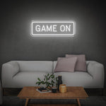 White GAME ON LED neon sign on the wall above a minimalist white couch with decor and table.