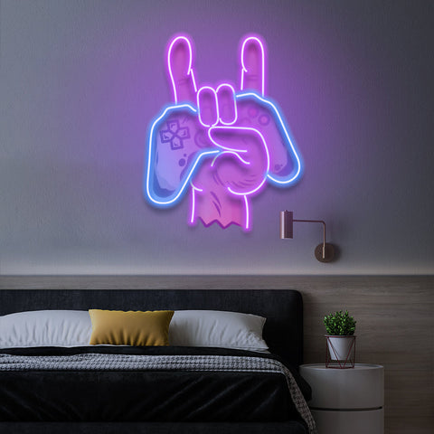 Gaming LED neon sign showing a 'rock on' hand gesture glowing in purple and blue, above a bed with a cozy pillow.