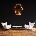 Orange Cake LED neon sign glowing on a dark wall in a modern lounge with stylish furniture and wooden flooring