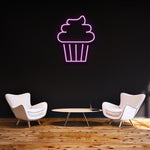 Pink Cake LED neon sign glowing on a dark wall in a modern lounge with stylish furniture and wooden flooring