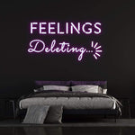 Purple neon sign reading 'Feelings Deleting' displayed above a modern bed on a black wall, ideal for bedroom decor.