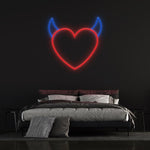 Red neon heart with blue devil horns displayed above a modern bed on a black wall, perfect for unique bedroom wall decor or themed spaces.