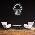 White cake LED neon sign glowing on a black wall, paired with modern furniture and a clean minimalist setup.