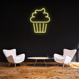 Yellow cake LED neon sign on a black wall, styled with modern white chairs and wooden flooring, perfect for contemporary interior design.